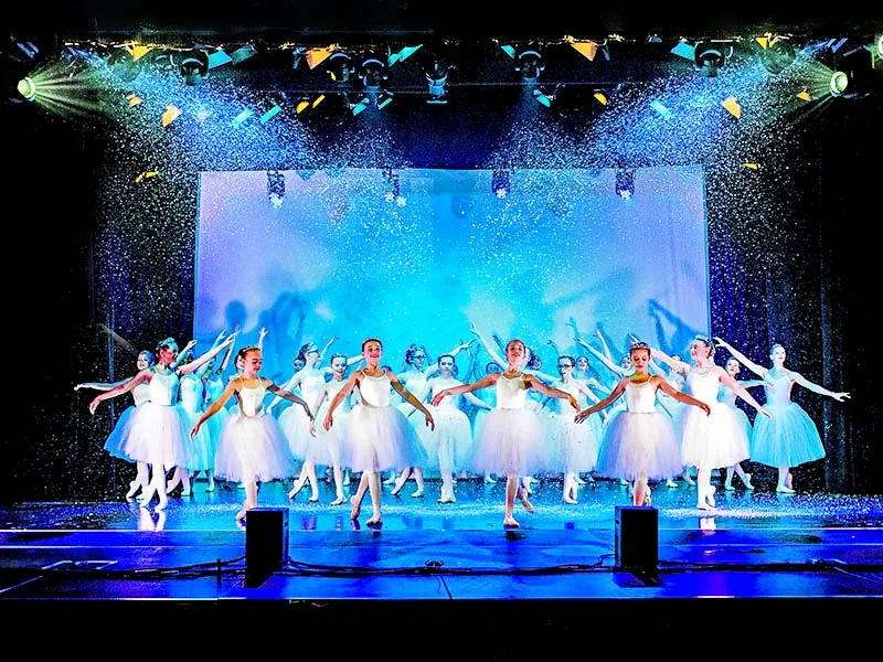 dance school show ballet dancers on stage in white costumes as snow falls through stage lights