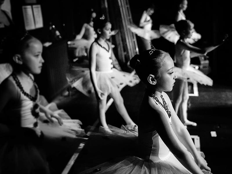 monotone photo of young dancers in ballet costume waiting in wings to go onstage