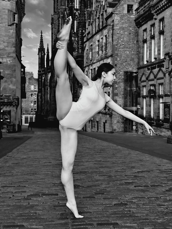 monochrome photo of dancer in white leotard posing on deserted street near Edinburgh Castle esplanade Scotland