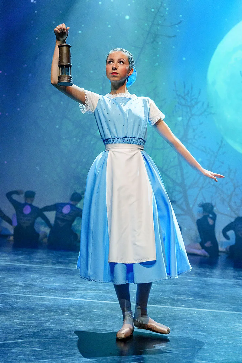 beautiful atmospheric moment as dancer in pinafore dress holding lantern stands on moonlight stage set captured by professional dance show photographer